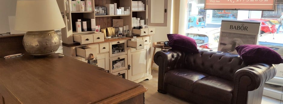 Empfangsbereich des Instituts mit lederner Chesterfield-Couch, Produktregal und Blick durch das Schaufenster auf die Kurfürstenstraße